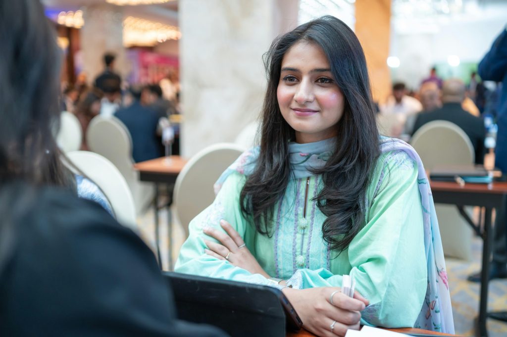 A young woman in traditional Pakistani clothing attends a lively business networking event indoors.